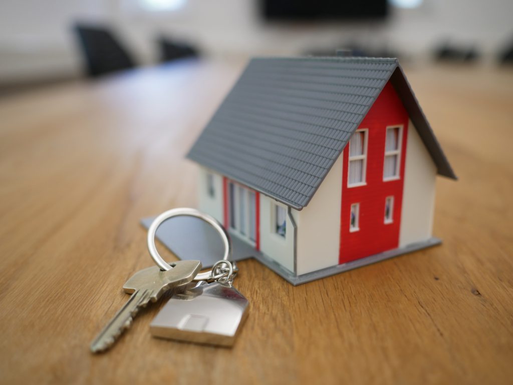 Trousseau de clés posé sur une table en bois à côté d'une maison miniature rouge, blanche et grise