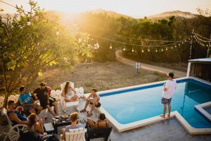 extérieur de maison avec piscine et guirlande lumineuse avec des personnes assises qui prennent un verre