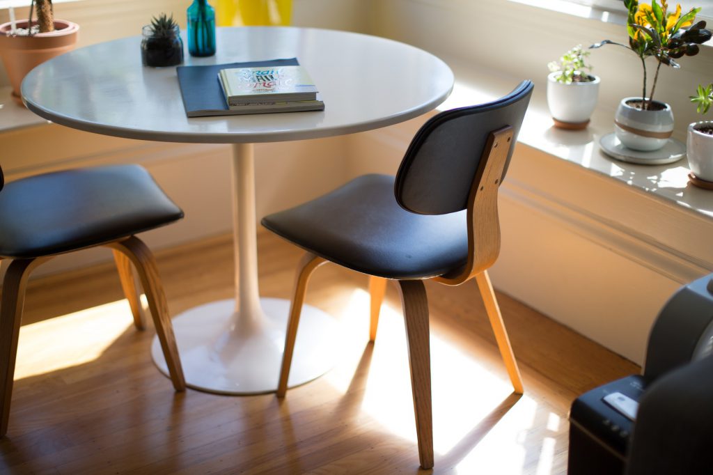 Salle à manger avec une table ronde en verre et deux sièges noirs disposés dans l'angle d'une pièce ensoleillée